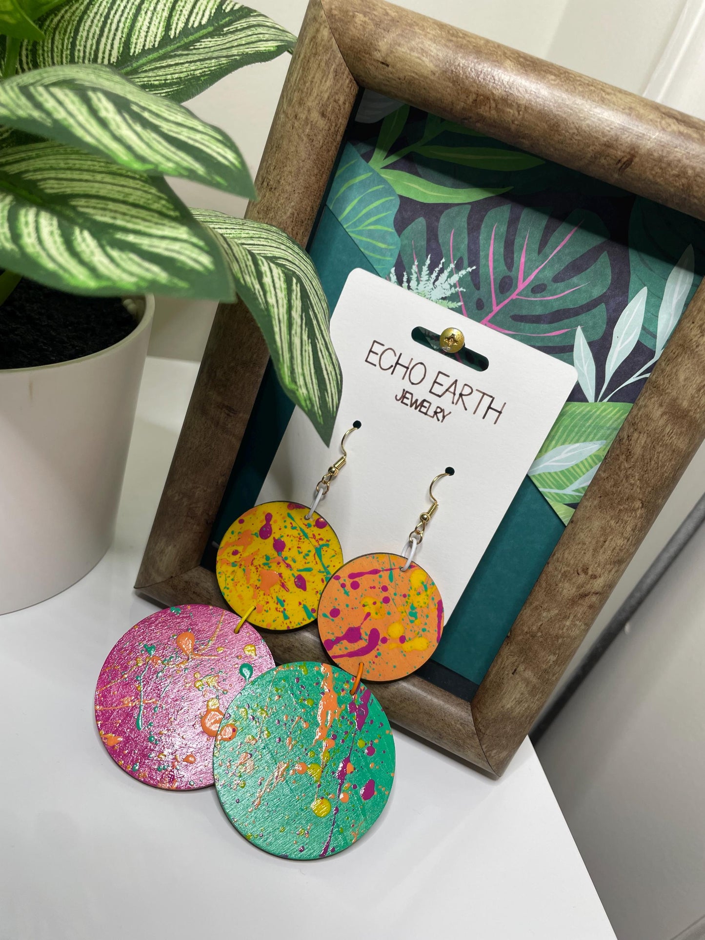 Colorful earrings on a 'Echo Earth' branded card with a plant in the background