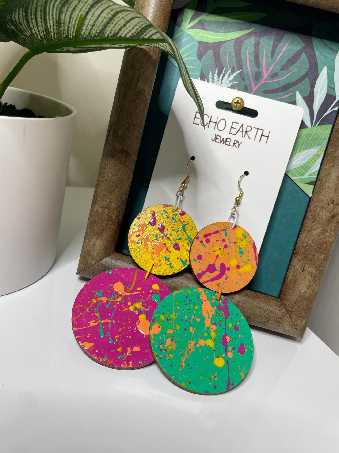 Colorful earrings on a Echo Earth Jewelry card with a plant and wooden frame in the background.