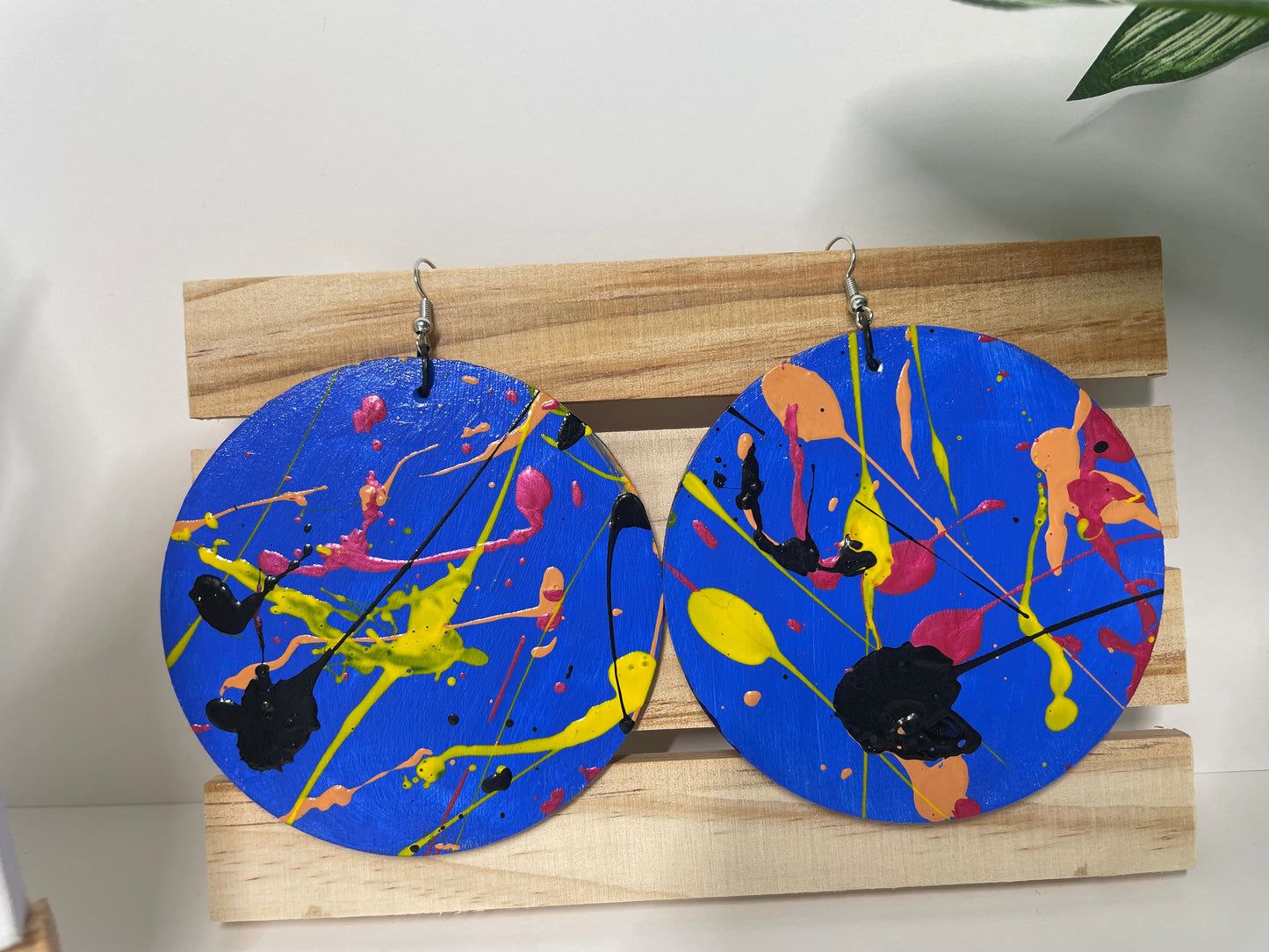 Pair of round earrings with colorful paint splatter design on a wooden stand.