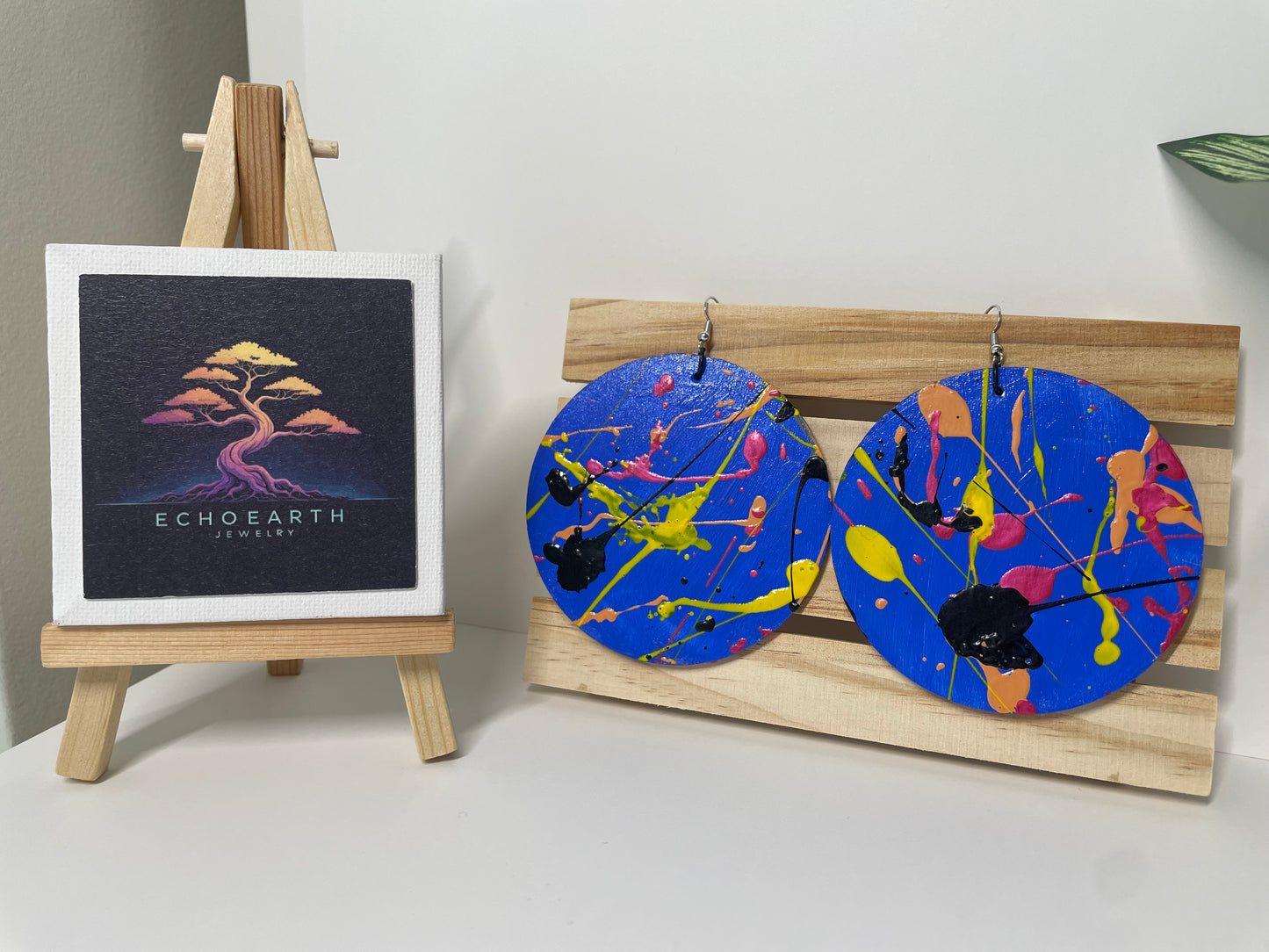 Colorful earrings on a wooden stand with a small easel displaying a card labeled 'ECHOEARTH'.