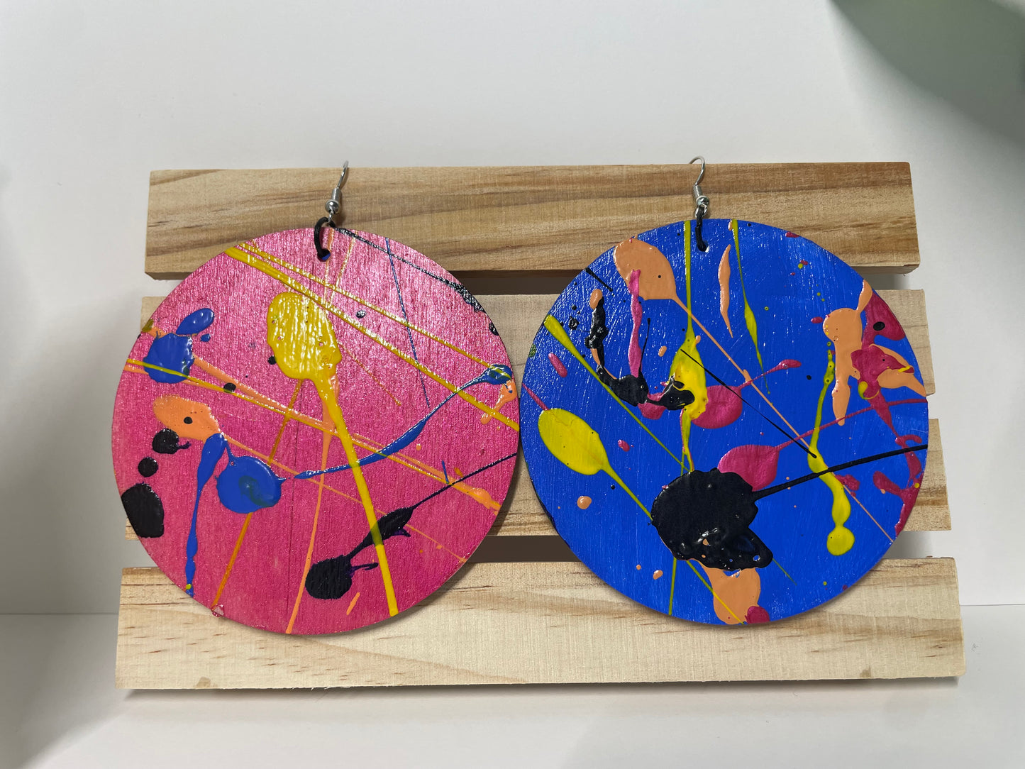 Pair of colorful abstract earrings on a wooden stand.