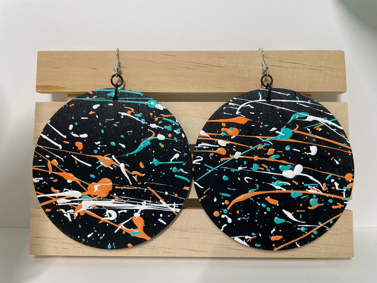 Pair of round earrings with a colorful abstract design on a wooden stand.