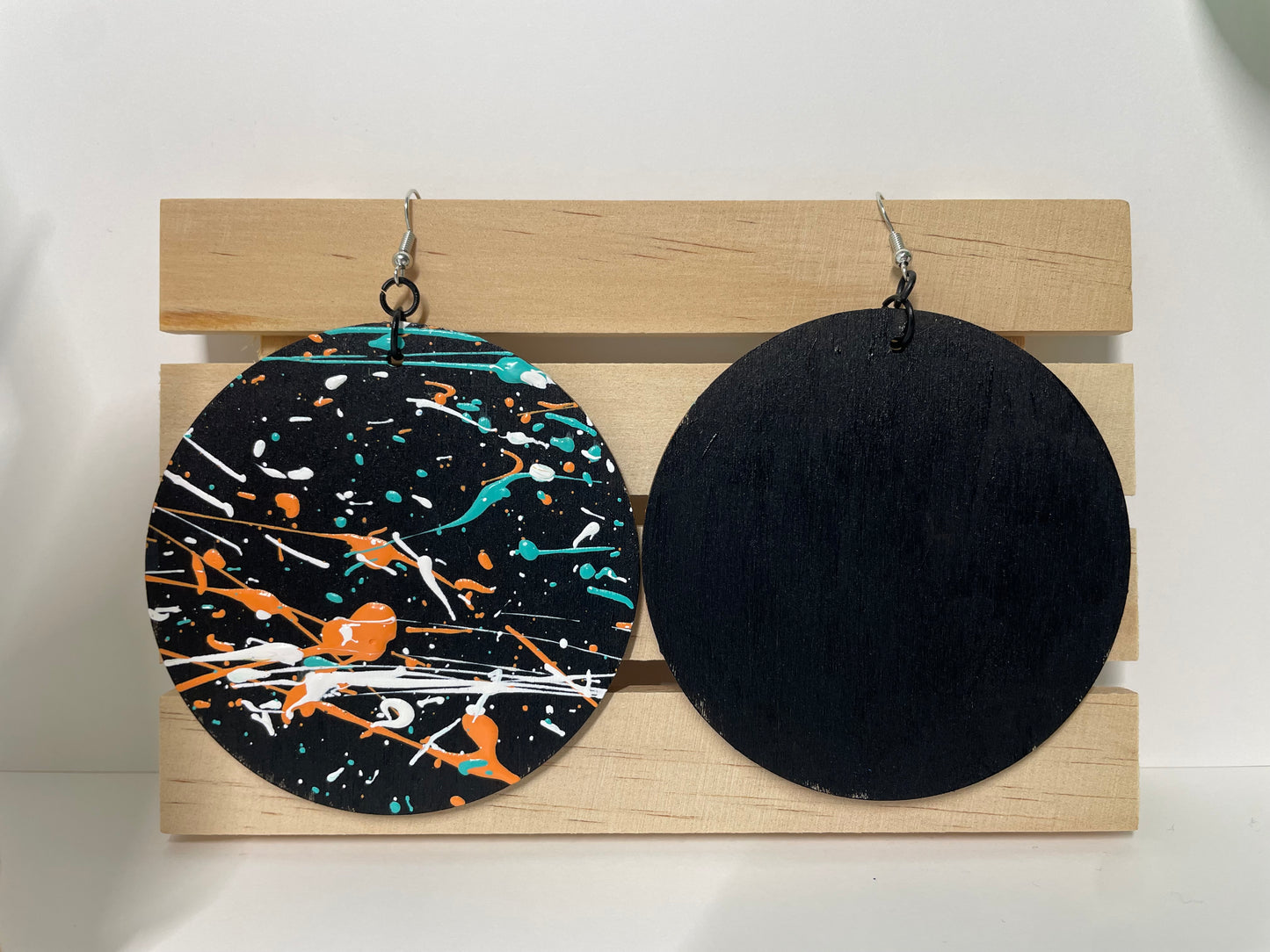 Two pairs of earrings on a wooden display board, one with black and multicolor design, the other solid black.
