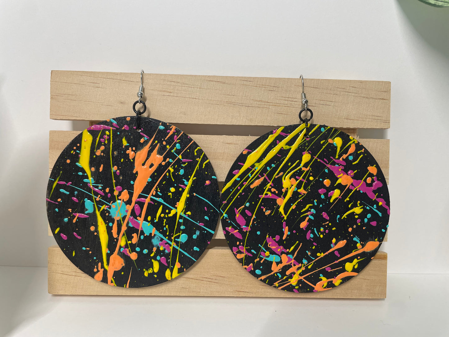 Colorful splatter-patterned earrings on a wooden stand against a white background