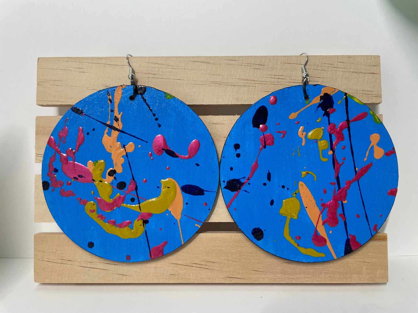 Pair of blue circular earrings with colorful abstract designs on a wooden stand.